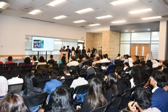 A formal audience of students in blazers seated for a presentation