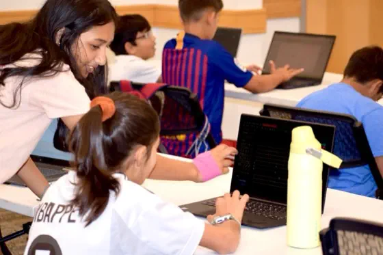 A volunteer leaning over to help a student with their laptop