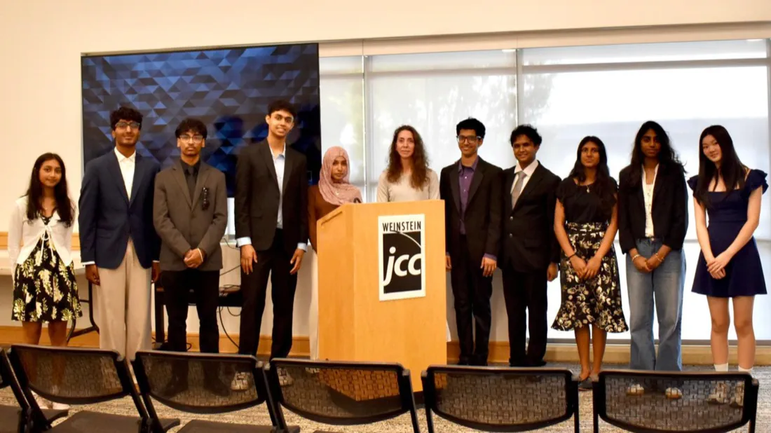 A group of students gathered around a table for a hands-on chemistry demonstration, a color-scale slide on the screen behind them
