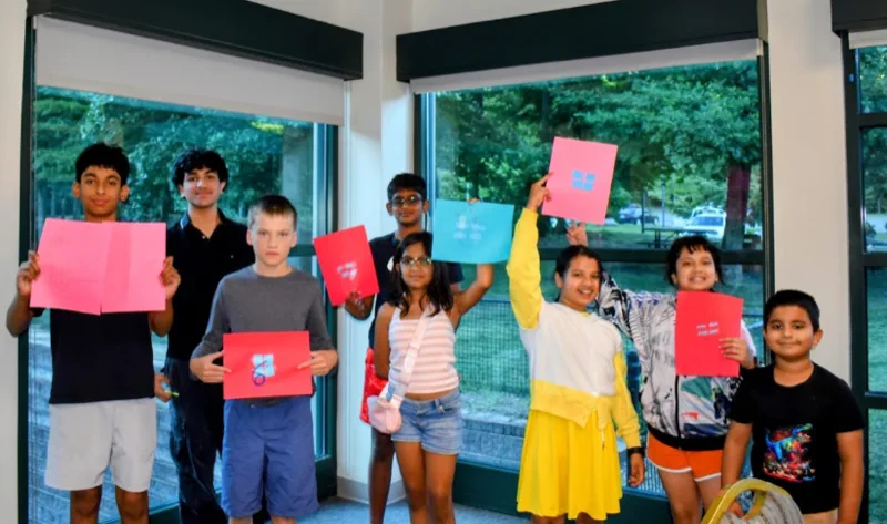 A group of students holding up colored worksheets they completed during a session