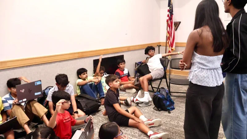Students sitting on the floor of a meeting room, listening as a volunteer speaks with them