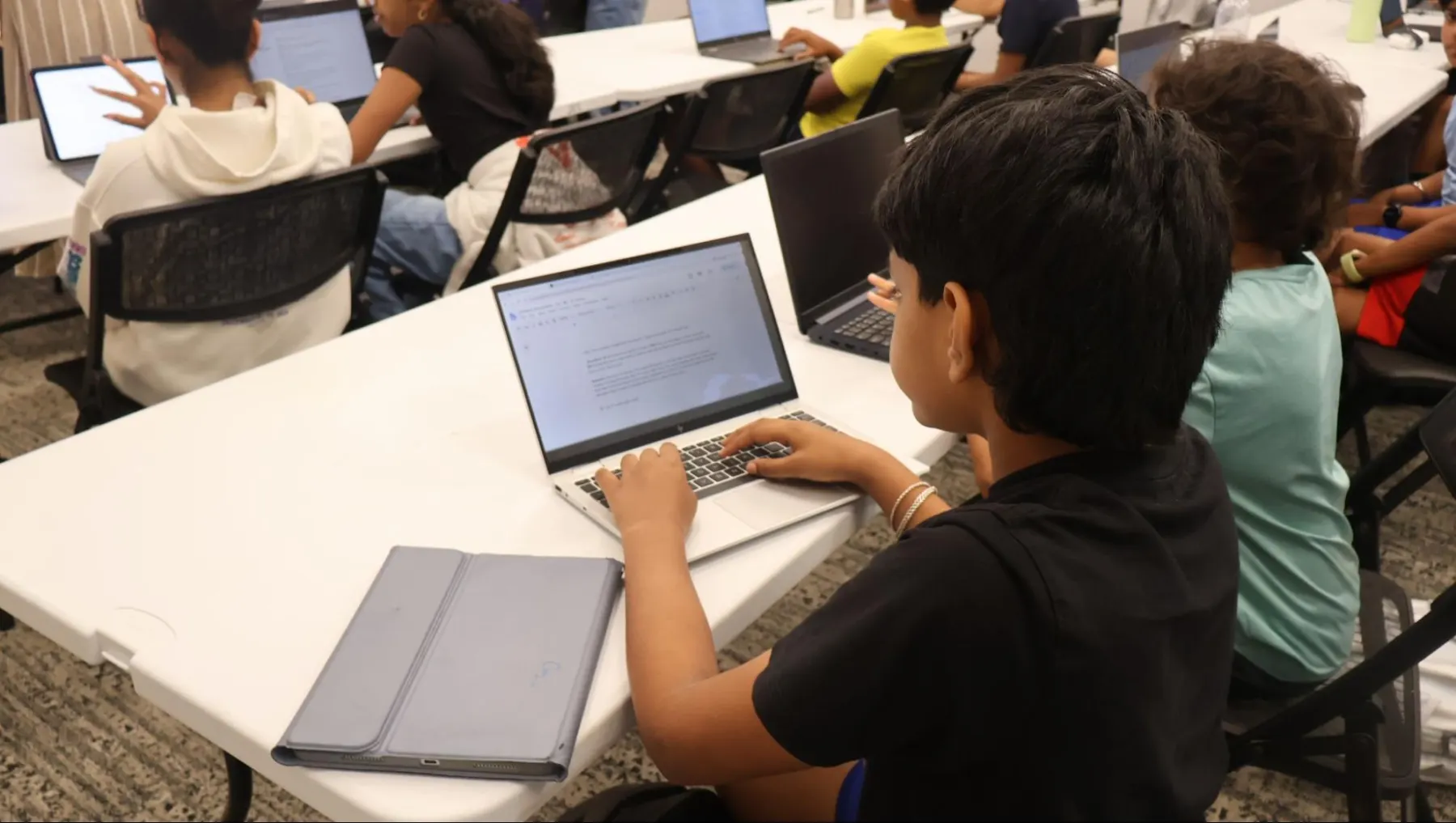 A student working on a laptop beside classmates during a session