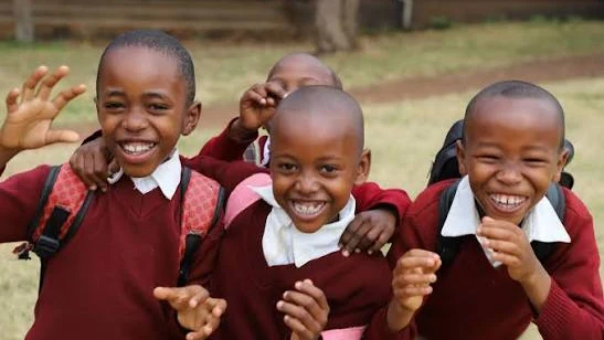 Students in Kenya smiling and raising their hands outside their school