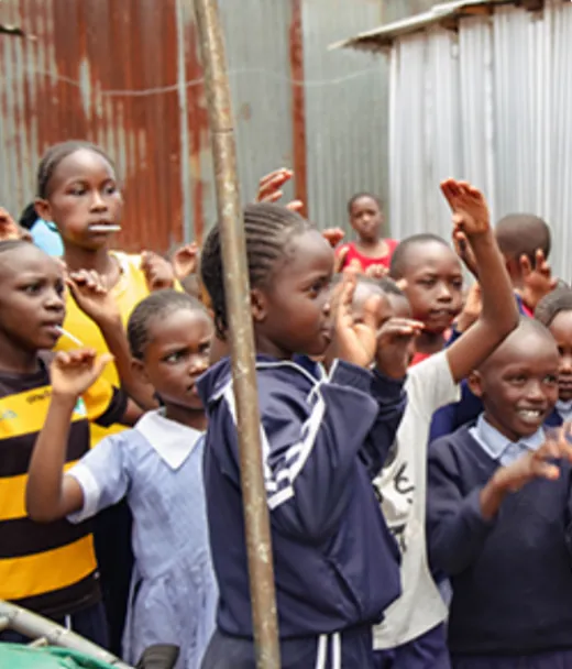 Young students in school uniforms raising their hands outdoors in Kenya