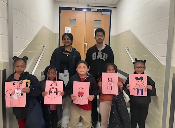 Students holding up their artwork with two volunteers in a school hallway