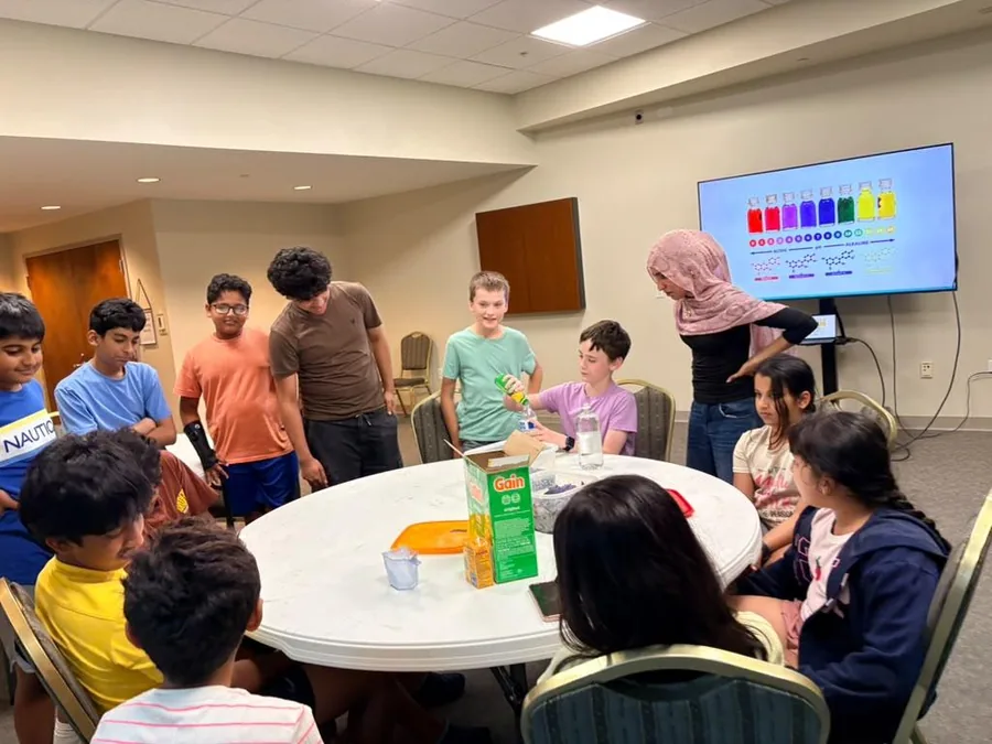 Students gathered around a table working through a hands-on activity with a volunteer